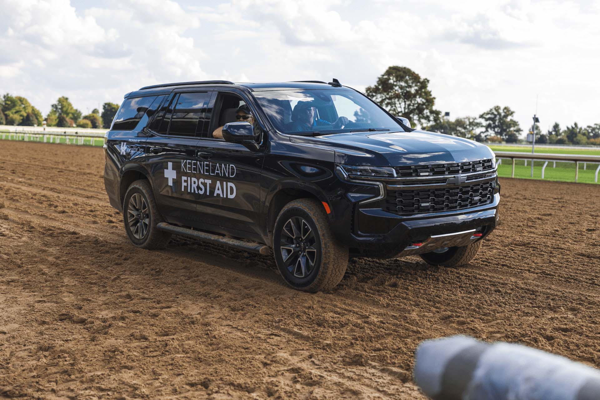 A picture of the Horseracejockey First Aid car on the dirt track. It is a large black Chevy SUV.